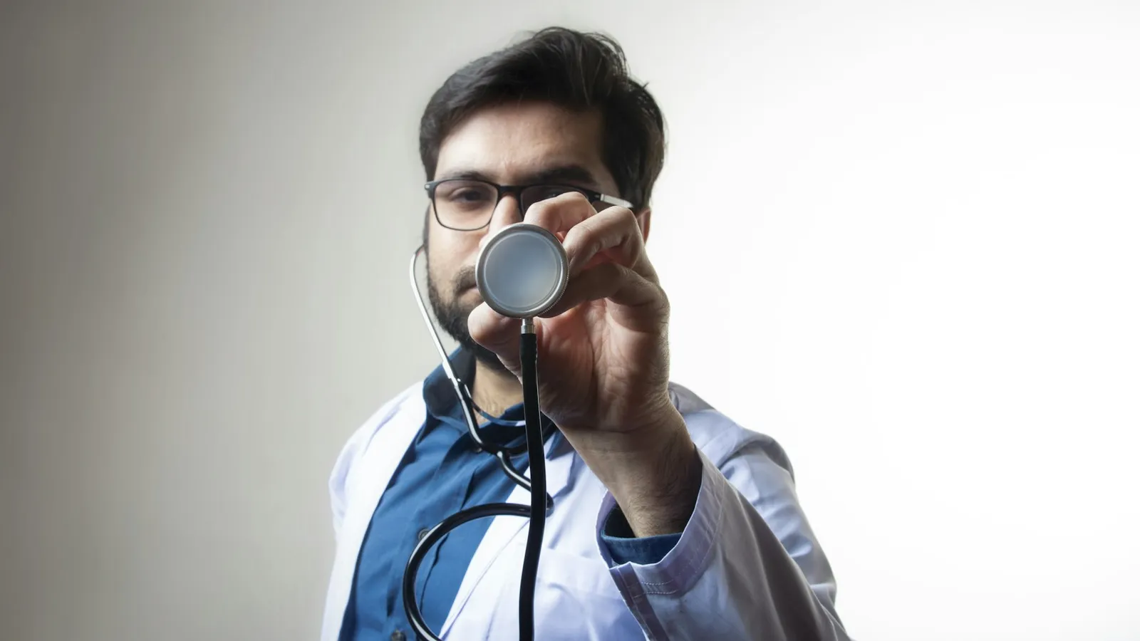 Médico segura o estetoscópio em direção à câmera, como se gravasse um vídeo educativo para as redes