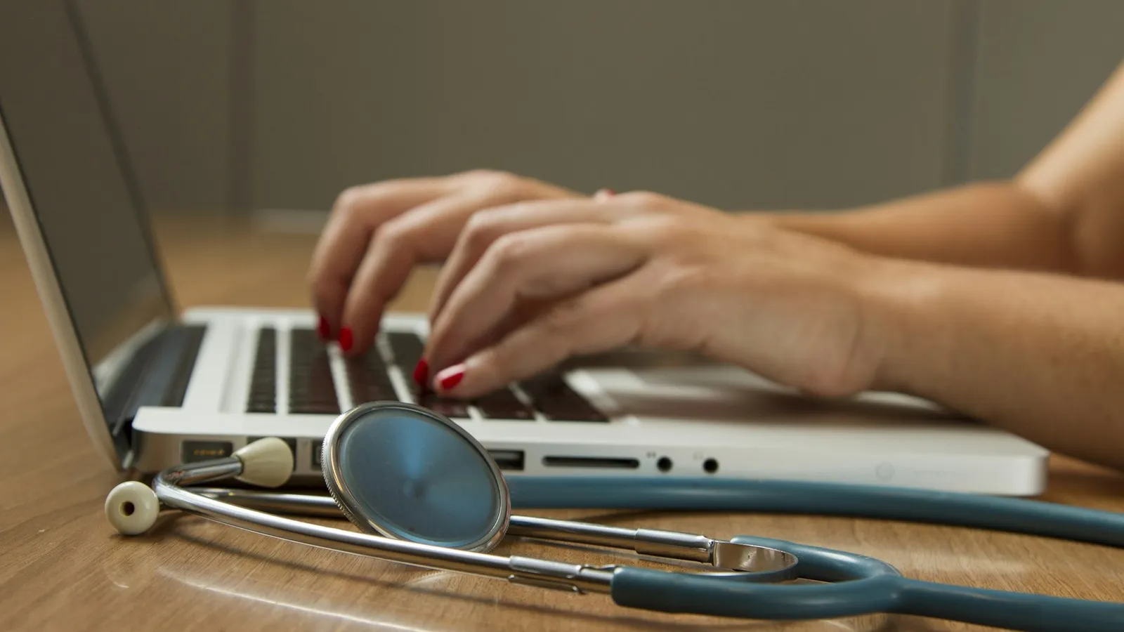 Mesa de consultório com notebook aberto e estetoscópio ao lado, representando a rotina de comunicação digital do médico